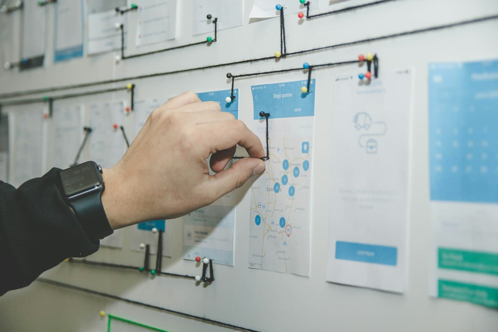 Hand pointing at app wireframes pinned to a planning wall